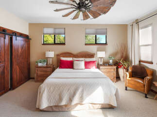 Experience rustic charm in this inviting bedroom featuring a grand wooden barn door and a striking windmill-inspired ceiling fan.