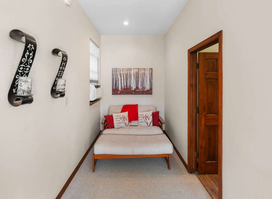 This hallway features a cozy seating area with a light-colored daybed adorned with red and patterned throw pillows, and a red throw blanket.