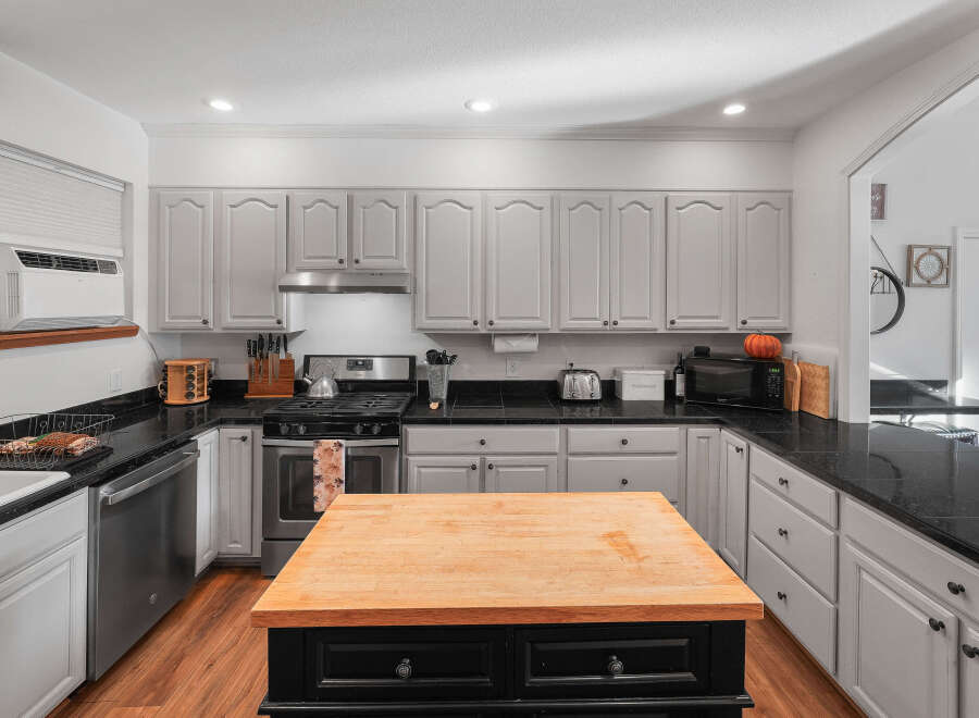This spacious kitchen boasts ample cabinet space with light gray finishes and black granite countertops, perfect for meal preparation.