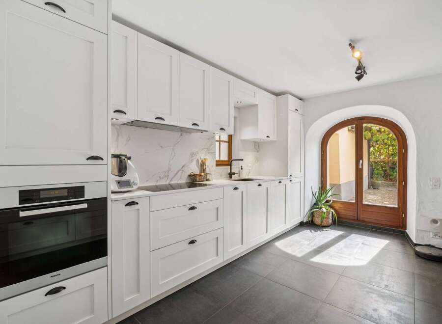 This modern white kitchen features sleek cabinetry, a marble-patterned backsplash, and integrated Miele appliances, including a built-in oven.