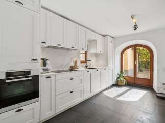This modern white kitchen features sleek cabinetry, a marble-patterned backsplash, and integrated Miele appliances, including a built-in oven.