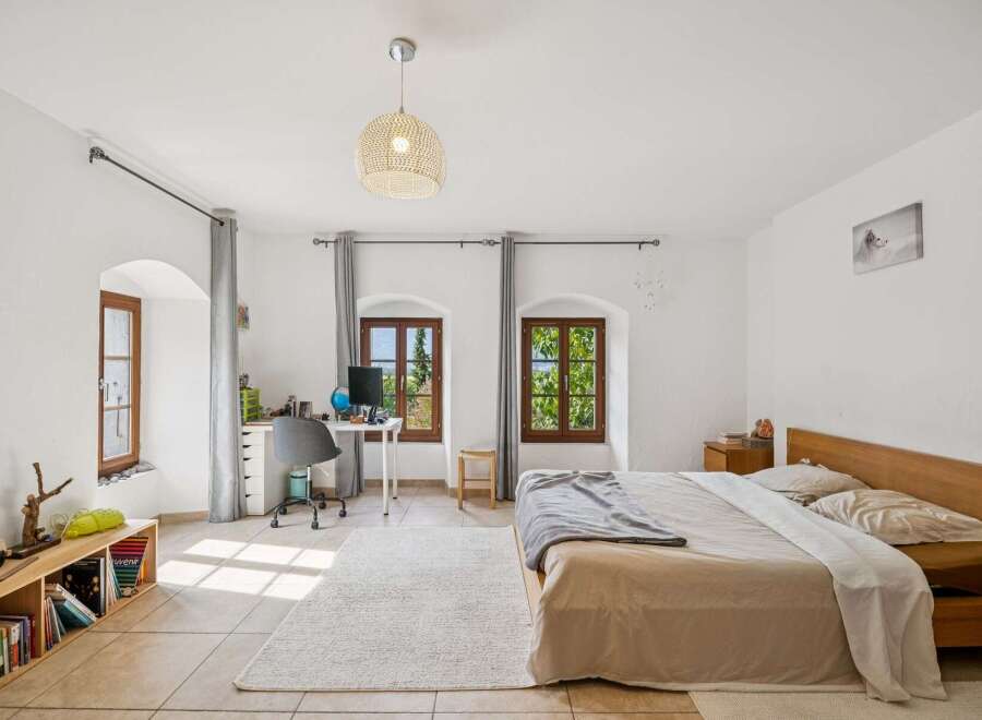 This bright and airy bedroom features a comfortable bed with a wooden headboard, perfect for restful nights.