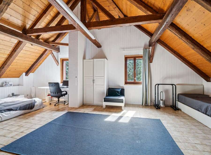 Discover this charming attic bedroom featuring exposed wooden beams and a sloped ceiling, creating a cozy and rustic ambiance.