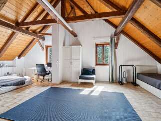 Discover this charming attic bedroom featuring exposed wooden beams and a sloped ceiling, creating a cozy and rustic ambiance.