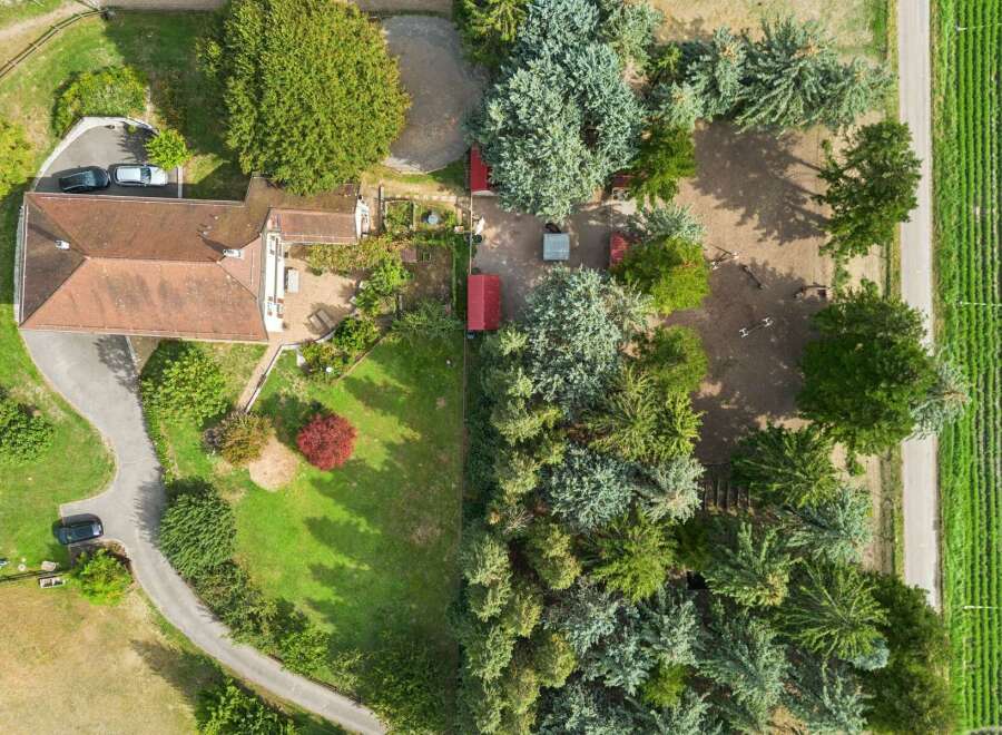 Discover this charming property featuring a spacious house with a red-tiled roof, surrounded by lush greenery and mature trees.