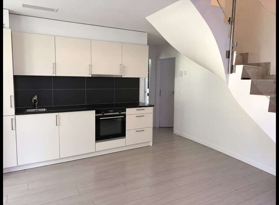 Discover modern living in this sleek kitchen featuring cream cabinetry, a striking black tile backsplash, and a built-in oven.