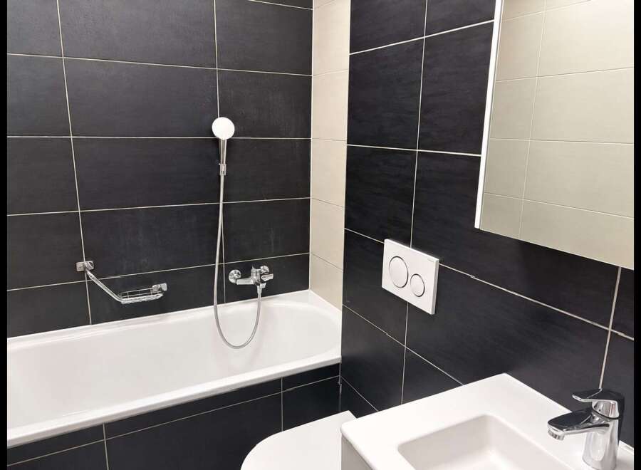 Experience modern comfort in this sleek bathroom, featuring a deep soaking tub with a chrome showerhead and a convenient soap dish.