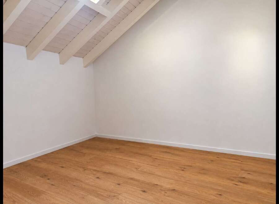 Experience the charm of this empty room, featuring a beautifully sloped ceiling with exposed wooden beams and a skylight that floods the space with natural light.