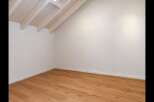 Experience the charm of this empty room, featuring a beautifully sloped ceiling with exposed wooden beams and a skylight that floods the space with natural light.