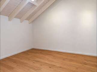 Experience the charm of this empty room, featuring a beautifully sloped ceiling with exposed wooden beams and a skylight that floods the space with natural light.