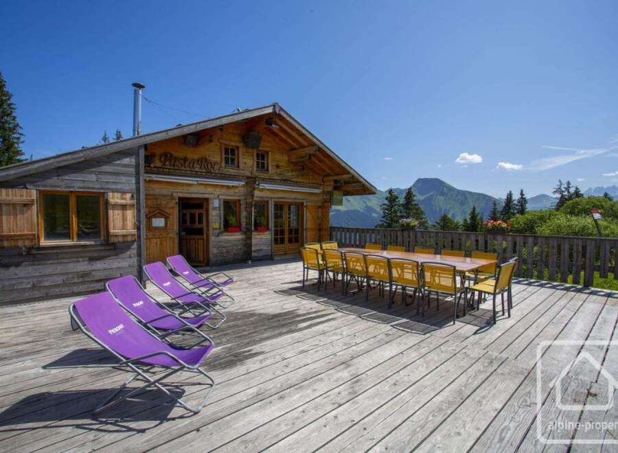 Enjoy breathtaking mountain views from the expansive wooden deck of this charming alpine chalet.