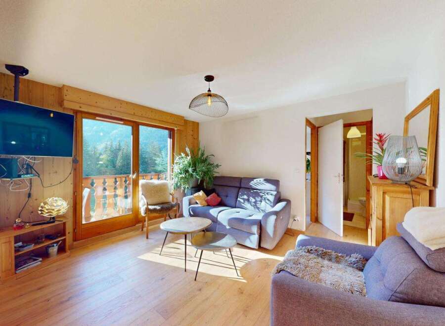 Experience breathtaking mountain views from this charming living room, featuring a cozy sofa and a large television mounted on a wooden accent wall.