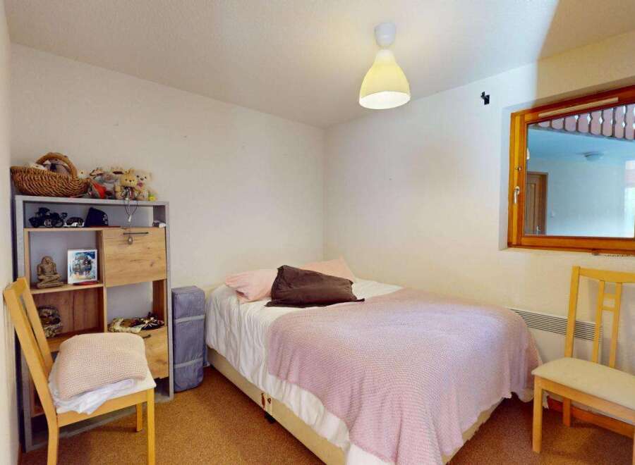 This cozy bedroom features a comfortable bed adorned with a pink throw blanket and plush pillows, perfect for relaxation.