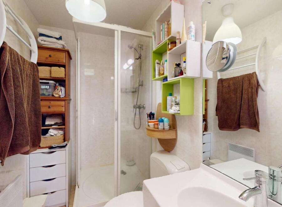 This compact bathroom maximizes space with a corner shower, a wall-mounted vanity with ample storage, and a tall linen cabinet.