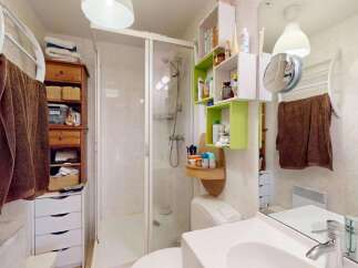 This compact bathroom maximizes space with a corner shower, a wall-mounted vanity with ample storage, and a tall linen cabinet.