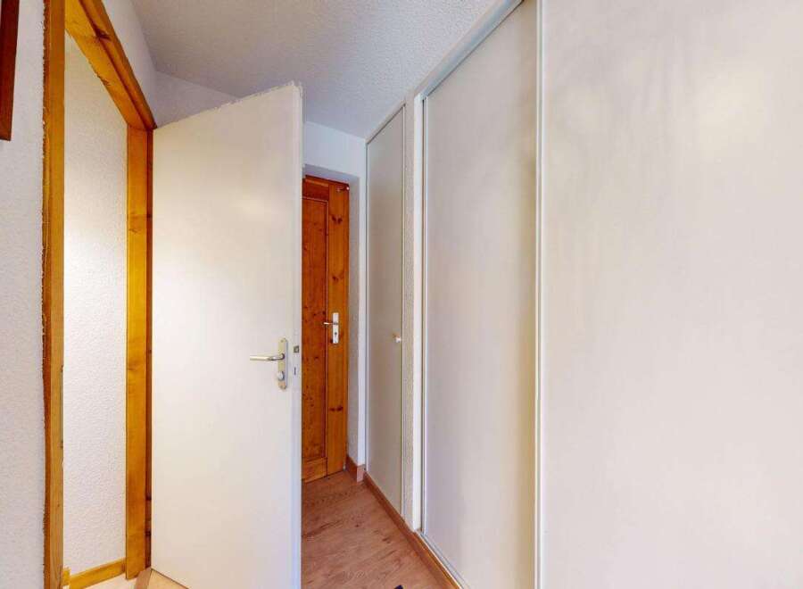 This hallway features a bright and airy feel, with a white door open to reveal a wooden interior door.