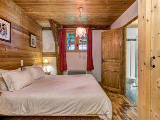 Experience rustic charm in this cozy bedroom featuring warm wooden walls and ceiling, complemented by a comfortable bed with crisp white linens.