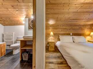 Experience rustic charm in this cozy bedroom featuring a comfortable bed with crisp white linens, complemented by warm wooden walls and ceiling.