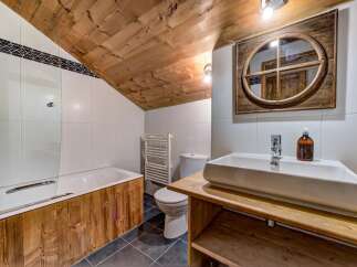 Experience rustic charm in this bathroom, featuring a wooden-paneled bathtub and a sloped, wood-planked ceiling that adds warmth and character.