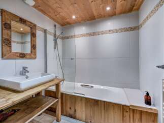 Experience rustic charm in this bathroom, featuring a wooden ceiling and a unique wooden-framed mirror above a modern white sink.