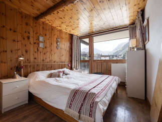 Experience cozy mountain living in this charming bedroom, featuring warm wood paneling on the walls and ceiling, and a comfortable bed adorned with a decorative throw.