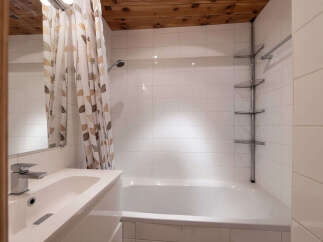 This bathroom features a clean and modern design with white tiled walls and a white bathtub.