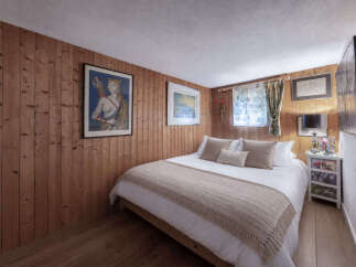 Experience cozy living in this charming bedroom, featuring warm wood-paneled walls and a comfortable bed adorned with plush pillows and a knitted throw.
