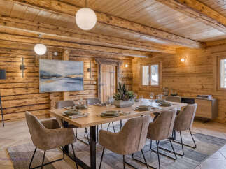 Experience rustic elegance in this stunning log cabin dining room, featuring a large wooden table set for eight with plush taupe chairs.