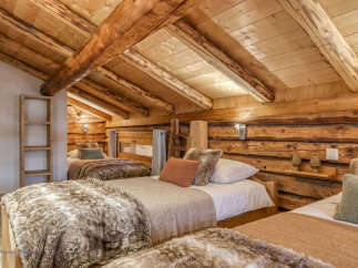 Experience rustic charm in this cozy attic bedroom, featuring exposed wooden beams and log walls that create a warm, inviting atmosphere.