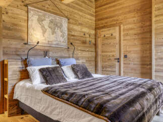 Experience rustic charm in this cozy bedroom, featuring warm wooden walls and a comfortable bed adorned with plush throws and pillows.