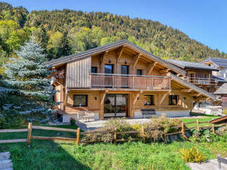 Experience the charm of this stunning wooden chalet nestled against a backdrop of lush green mountains.