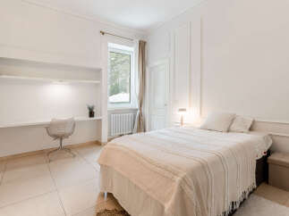 This bright and airy bedroom features a comfortable bed with plush pillows and a textured throw blanket, perfect for relaxation.