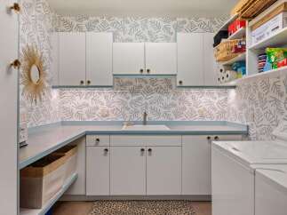 This laundry room boasts a charming blue and white leaf-patterned wallpaper, complemented by sleek white cabinetry and a light blue countertop.