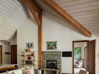 Experience rustic charm and modern comfort in this inviting living room, featuring a stunning stone fireplace and exposed wooden beams that soar across the vaulted ceiling.