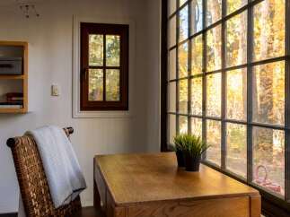 Enjoy the vibrant autumn foliage from this charming dining nook, complete with a rustic wooden table and a comfortable woven chair draped with a cozy blanket.