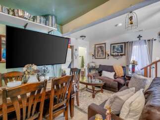 This cozy living and dining area features a large flat-screen TV mounted above a dining table with wooden chairs, perfect for family meals.