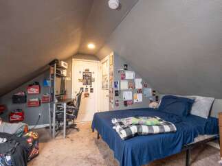Discover this charming attic bedroom, featuring a comfortable bed with navy blue linens and a cozy plaid blanket.