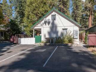 Discover this charming property featuring a white exterior with a vibrant green roof, set amidst a backdrop of lush pine trees.