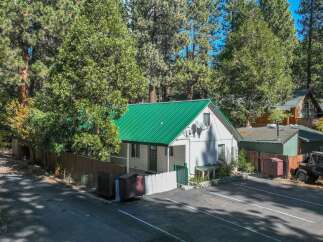 Nestled amongst tall pine trees, this charming white home features a vibrant green metal roof, offering a striking contrast against the natural landscape.