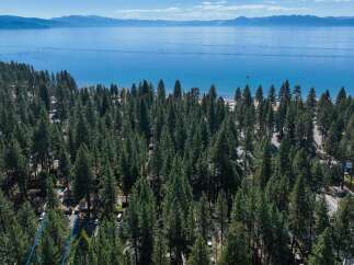 Experience the ultimate lakeside living with this stunning aerial view of a property nestled amongst tall pine trees, offering direct access to a pristine lake.