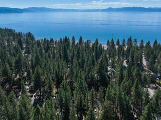 Experience the ultimate lakeside living with this stunning aerial view of a property nestled amongst tall pine trees, offering direct access to a pristine lake.