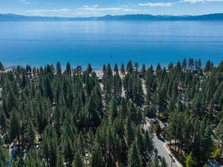 Experience the ultimate lakeside lifestyle with this stunning aerial view of a property nestled amongst towering pine trees, just steps from the crystal-clear waters of Lake Tahoe.