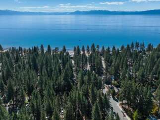 Experience the ultimate lakeside lifestyle with this stunning aerial view of a property nestled amongst towering pine trees, just steps from the crystal-clear waters of Lake Tahoe.