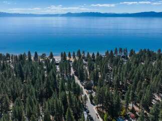 Experience the ultimate lakeside lifestyle with this stunning aerial view of a property nestled amongst towering pine trees, offering direct access to a pristine beach and the crystal-clear waters of Lake Tahoe.