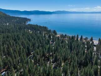 Experience the ultimate lakeside lifestyle with this stunning aerial view of a property nestled amidst a dense pine forest, offering direct access to a pristine beach and the sparkling blue waters of Lake Tahoe.