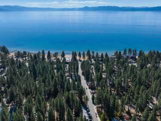 Experience the ultimate lakeside living with this stunning aerial view of a property nestled amongst lush pine trees, offering direct access to a pristine beach and the crystal-clear waters of Lake Tahoe.