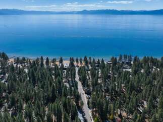 Experience the ultimate lakeside living with this stunning aerial view of a property nestled amongst lush pine trees, offering direct access to a pristine beach and the crystal-clear waters of Lake Tahoe.
