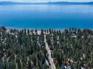 Experience the ultimate lakeside living with this stunning aerial view of a property nestled amongst lush pine trees, offering direct access to a pristine beach and the crystal-clear waters of Lake Tahoe.
