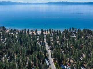 Experience the ultimate lakeside living with this stunning aerial view of a property nestled amongst lush pine trees, offering direct access to a pristine beach and the crystal-clear waters of Lake Tahoe.