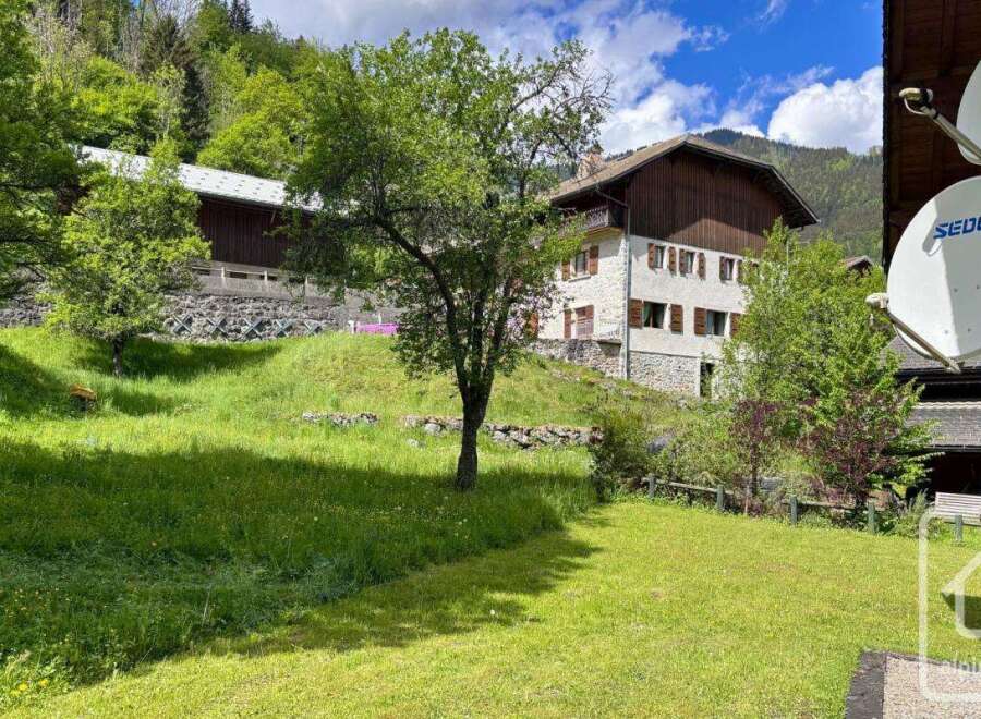 Nestled in a serene mountain landscape, this property offers a charming stone house with traditional wooden shutters, set against a backdrop of lush green hills and mature trees.